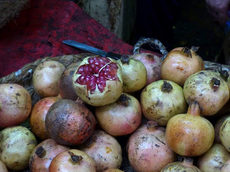 A full basket of pomegranates, some with green skins.