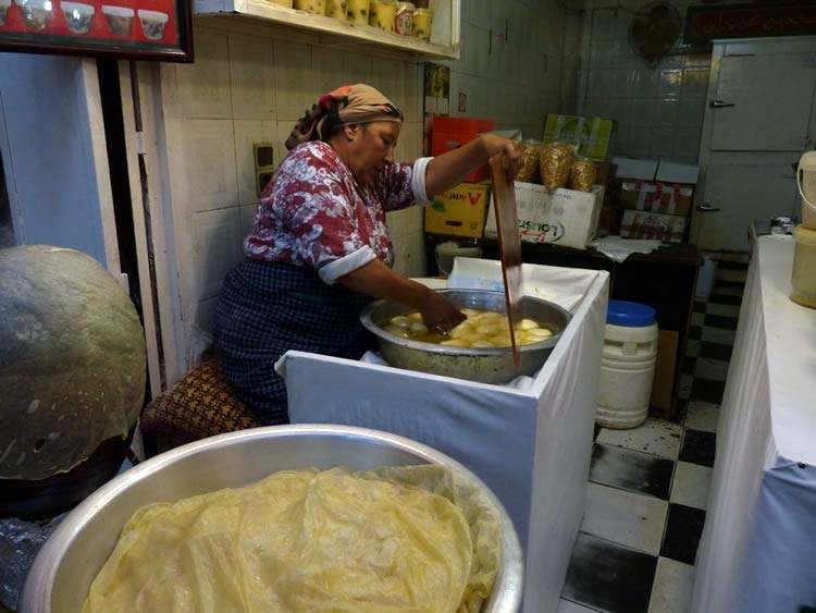 Dough in a large bowl with a cook in the back preparing individual flatbread.
              