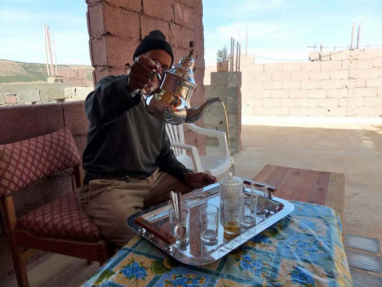 Man with large tea pot in his hand, pouring it into glasses.