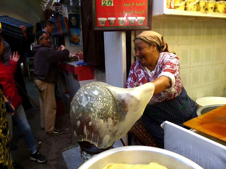 The cook stretches the dough paper thin and forms it on a shaped baking oven in the open market. 