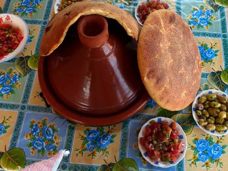 Moroccan flat bread wrapped around a clay cooker with a hole on top, surrounded by condiments.