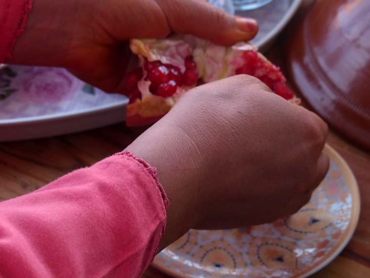 A closeup of hands breaking a pomegranate into pieces, surrounded by ornate patterned plates.