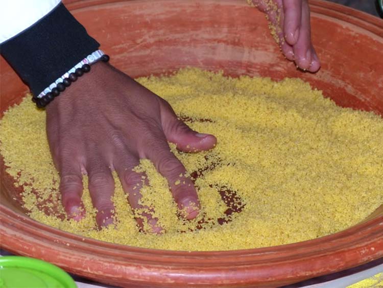 Chef preparing couscous in large round clay platter.