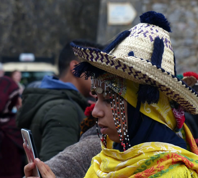 Moroccan Woman with bright yellow wrap and a straw hat with colorful beads hanging near her face.
                      