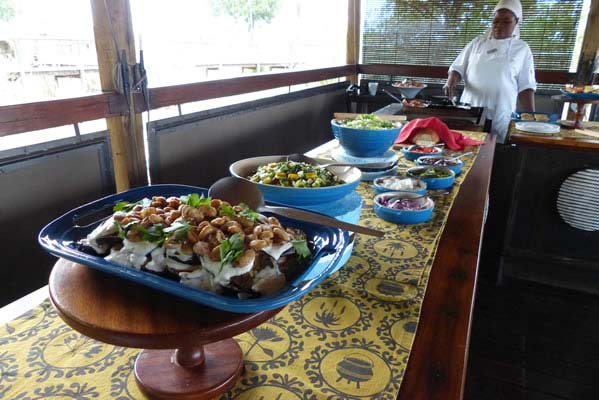 A bountiful table of food prepared buffet style with an African server standing nearby.