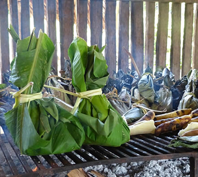 Packets of steamed food on open grill.