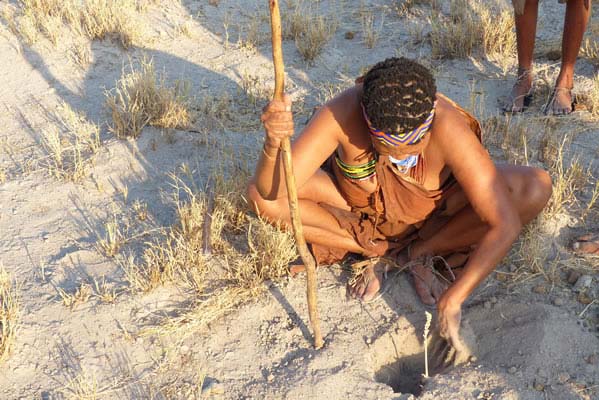 African native sitting over a hole dug in the sandy soil.