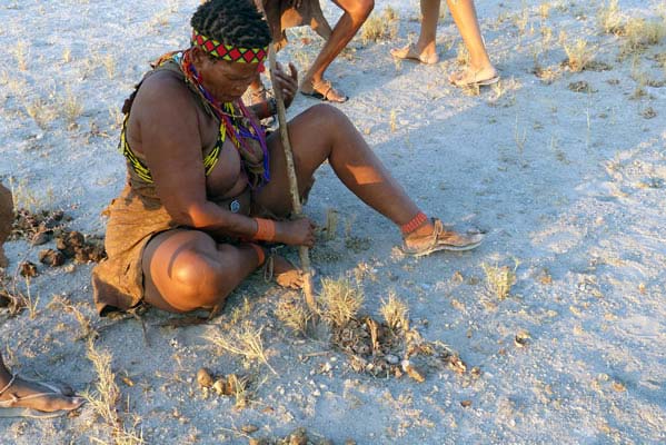 Native African sitting on ground with stick in full tribal attire.