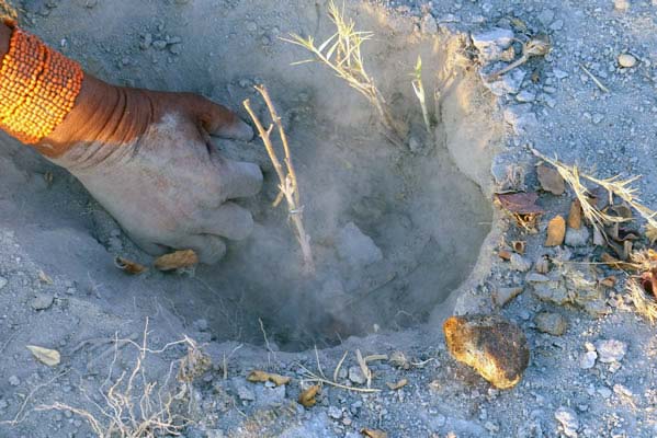 African tribal member's hand digging in a dusty hole.