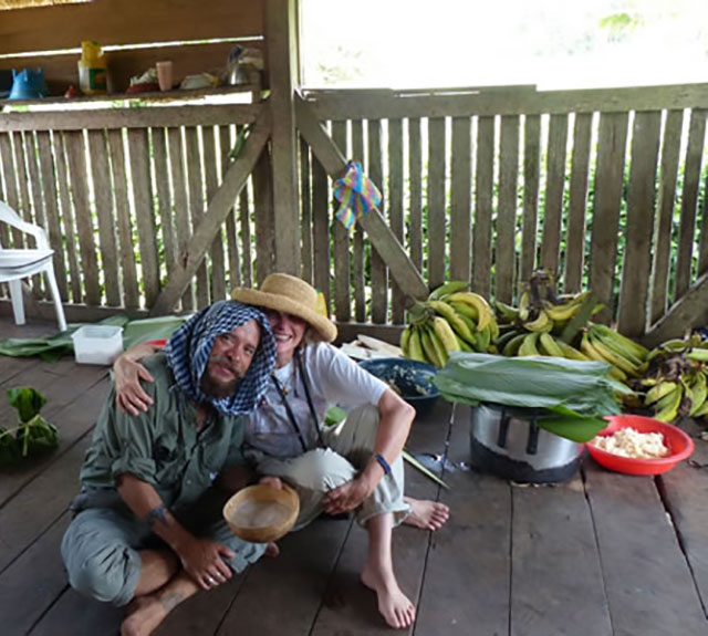 Nancy with a friend in a wood hut surrounded by tropical fruit.