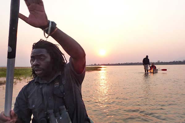 An African man rowing his canoe with others behind.