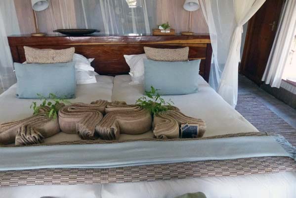 The elegant bedroom suite at camp with shiny dark wood headboard and towel sculpture on the bed.