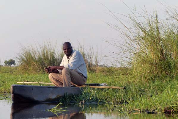 African man in boat surrounded by water, grass and the horizon.