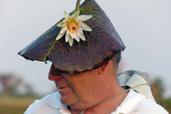 A close up of a male safari traveler wearing an African lily pad leaf as a hat, with a flower attached.