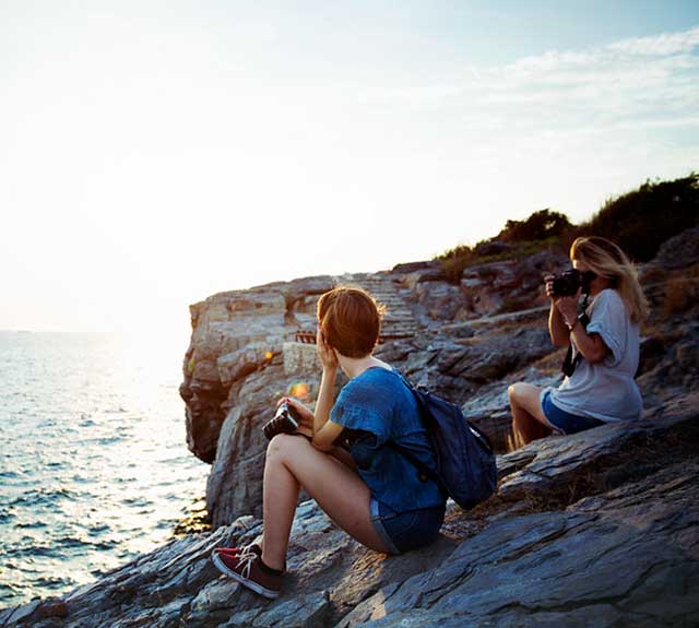 Women sitting on rock next to water. 